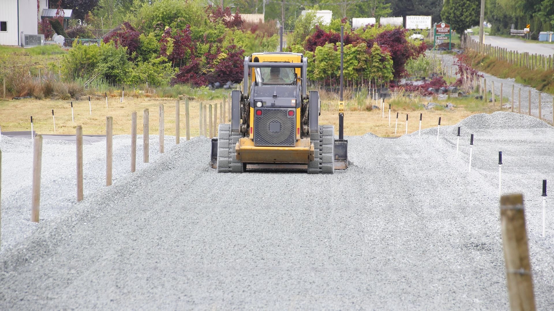 Yellow skid steer loader working on gravel road between wooden posts