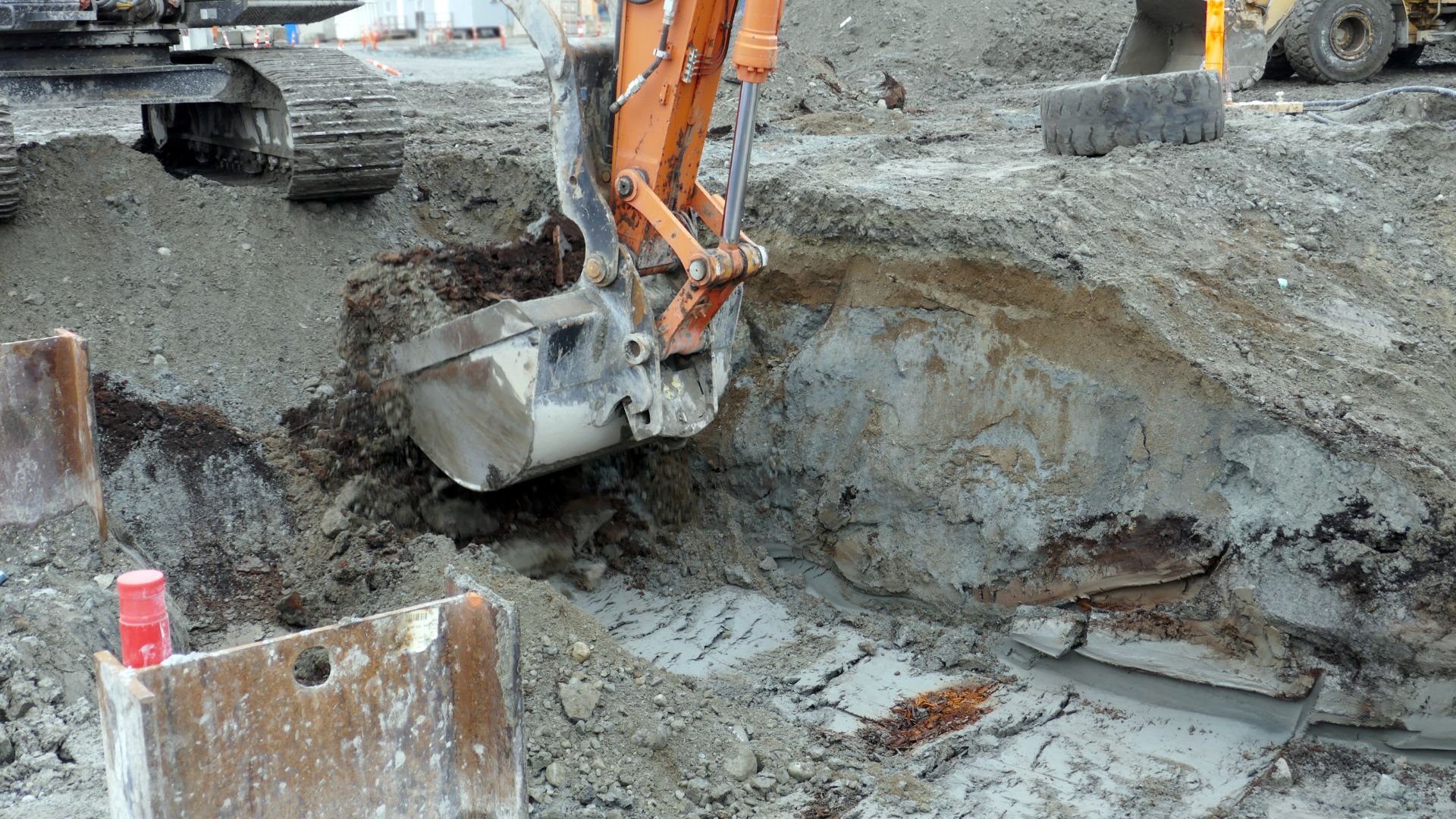 Orange excavator digging into muddy construction site with heavy machinery