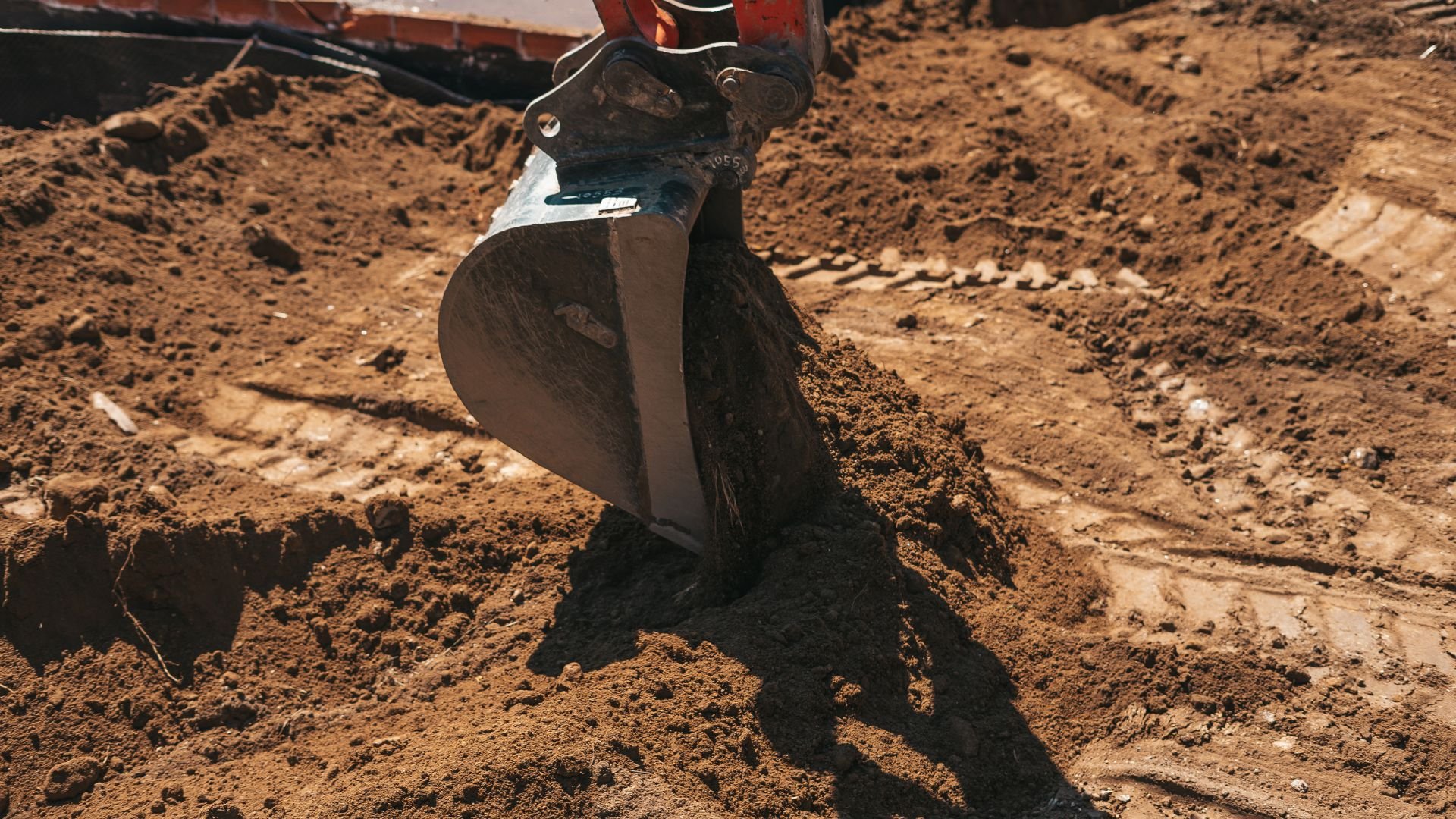Excavator bucket digging into dry, rocky soil at construction site