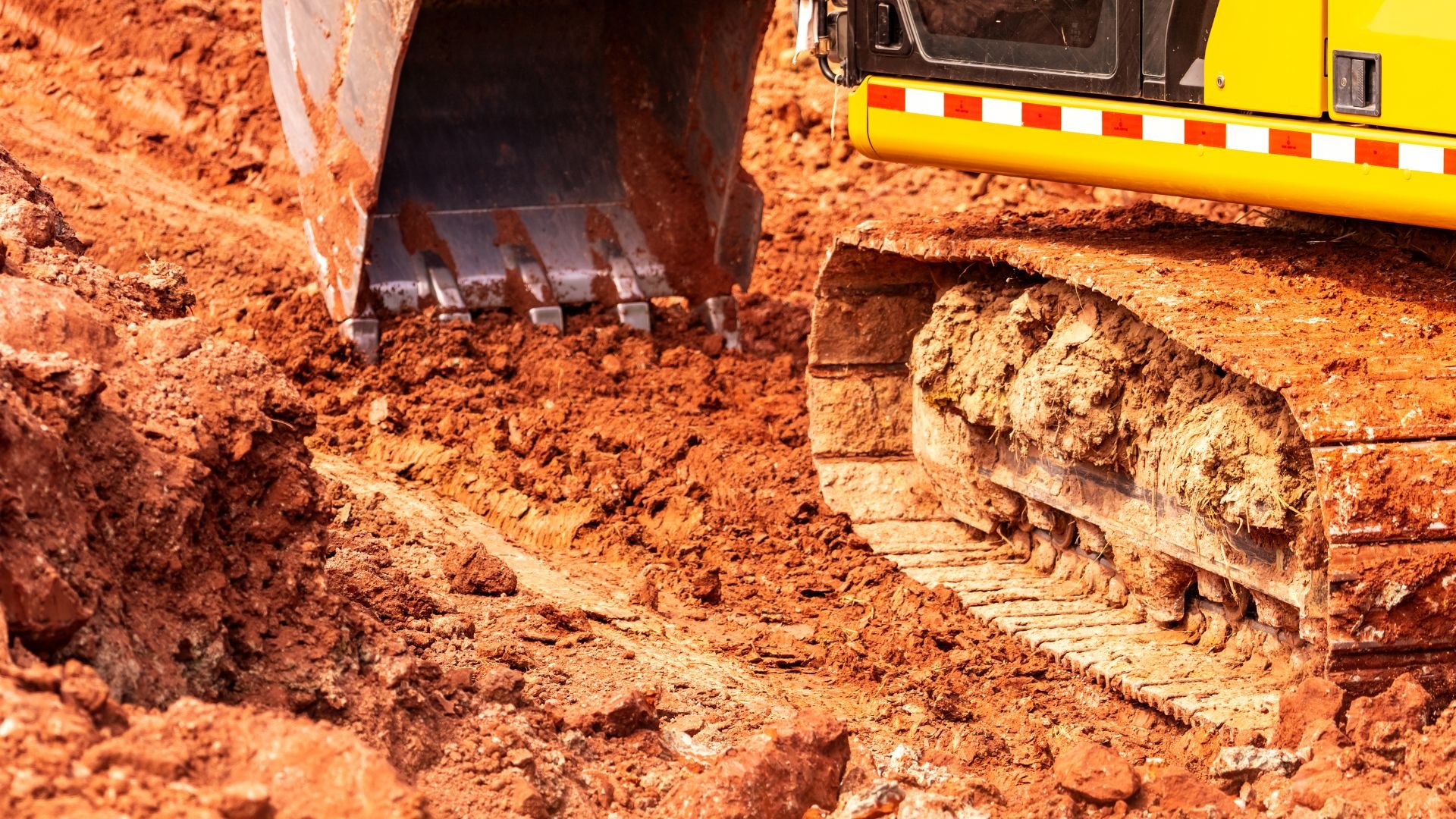 Yellow excavator digging in red clay soil on construction site
