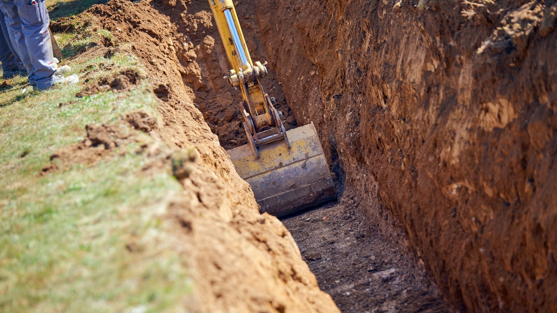 Excavator digging a deep trench in brown earth with grass nearby