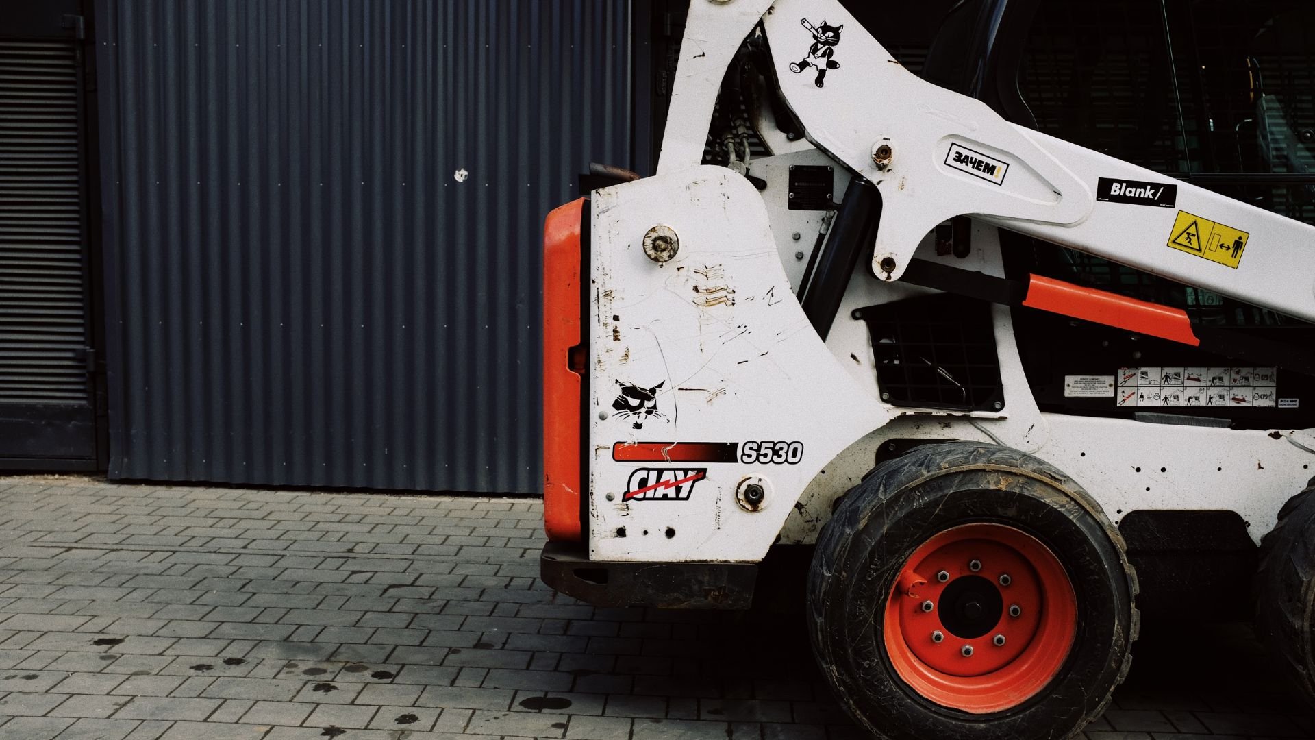 White and red Bobcat S530 skid-steer loader parked near corrugated wall
