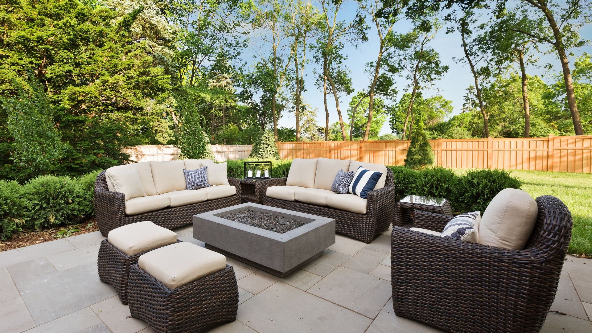 Luxurious outdoor patio with woven furniture and fire pit surrounded by trees