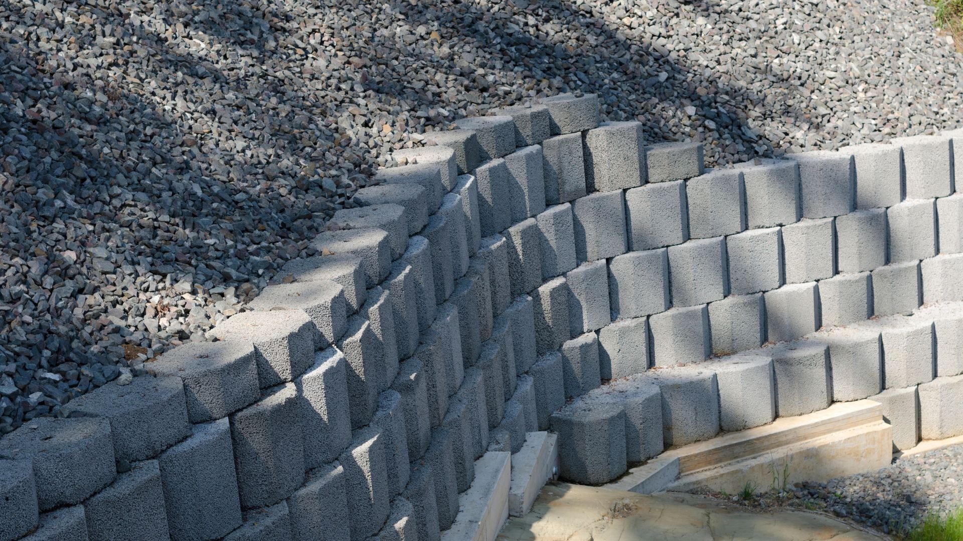 Curved concrete retaining wall with gray blocks surrounded by gravel
