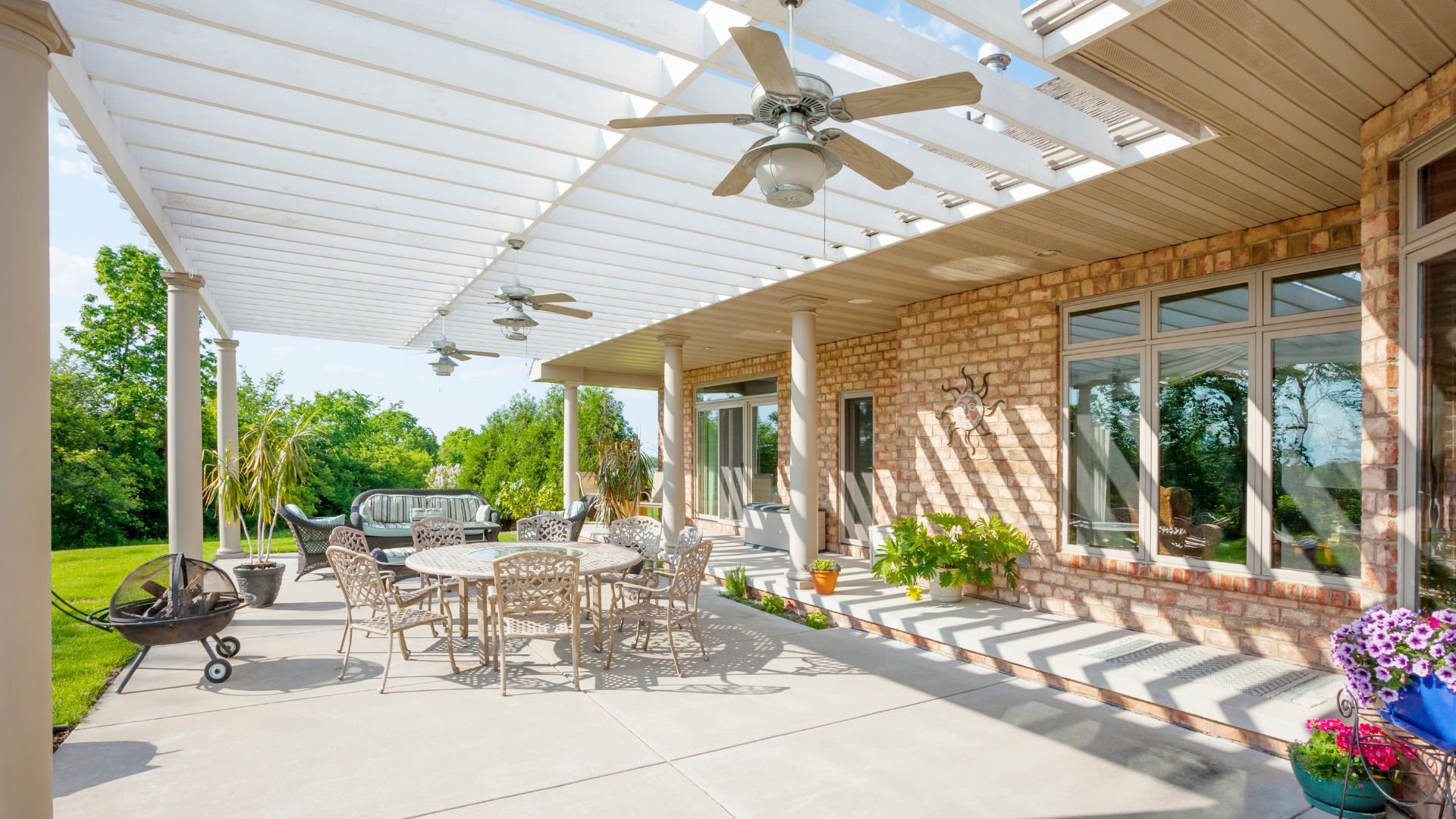 Spacious covered patio with outdoor furniture, fans, and potted plants