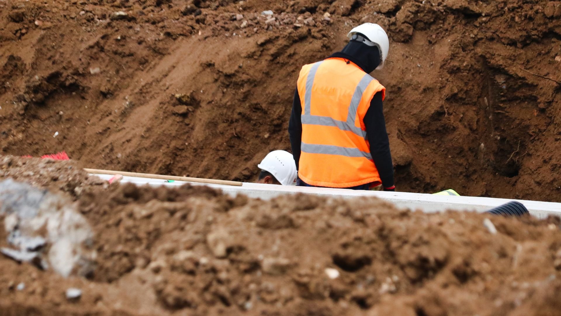 Construction workers in safety vests and hard hats digging in muddy excavation site